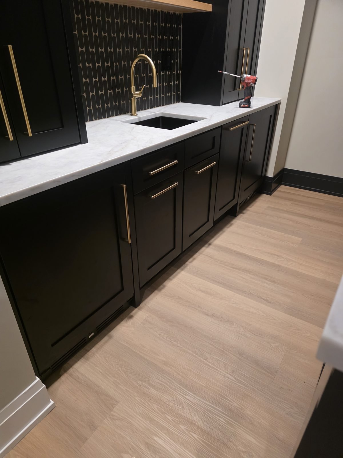 Black bar cabinetry with brass hardware and a marble countertop